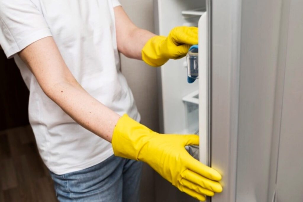 A Person in Yellow Gloved Hands Cleaning a Fridge